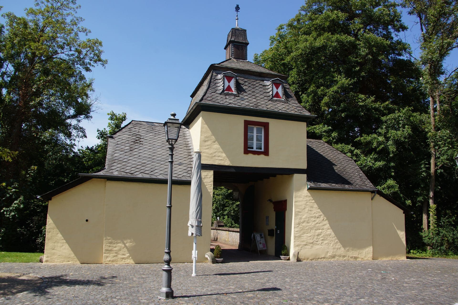 Torhaus von Schloss Eulenbroich in Rösrath, das Wahrzeichen der Stadt mit gelber Fassade und schiefergedecktem Turm