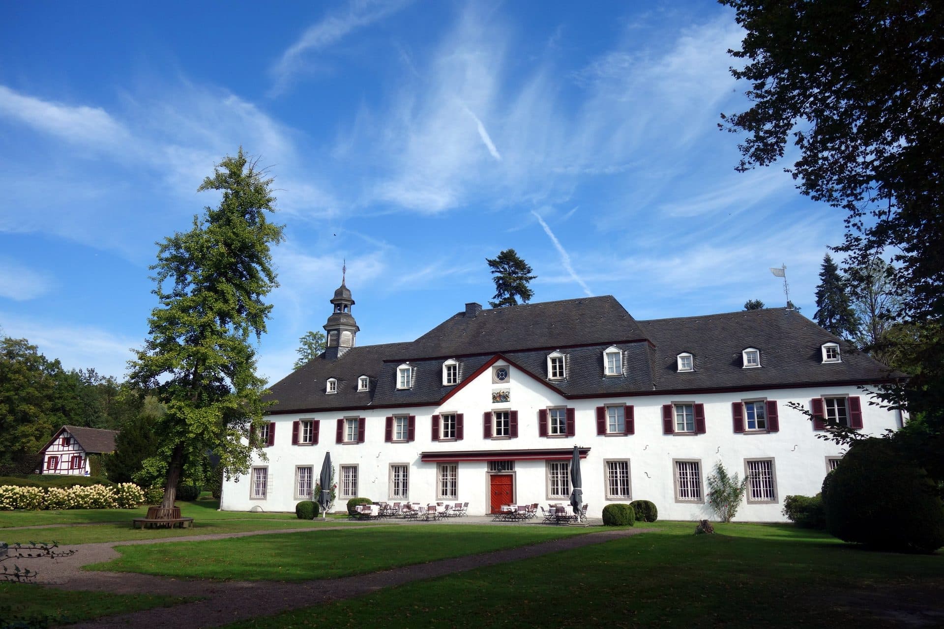 Schloss Auel in Lohmar-Wahlscheid, barockes Wasserschloss mit weißer Fassade und Glockentürmchen unter blauem Himmel
