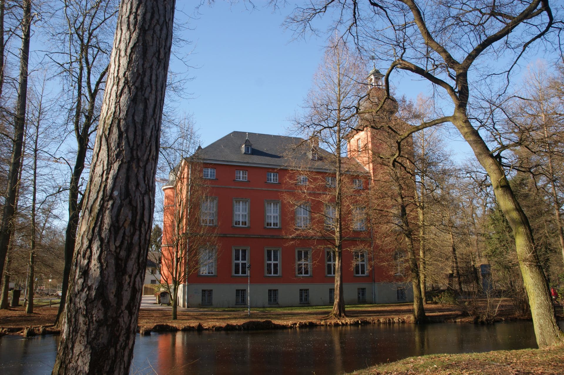 Burg Wissem in Troisdorf, das rote klassizistische Herrenhaus mit Turm, gespiegelt im Wassergraben des Burgparks